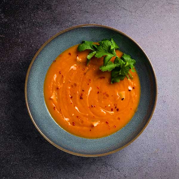 Tomato soup with an herb garnish in a black bowl.